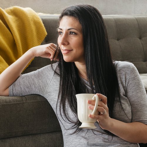 Woman leaning on couch holding mug.